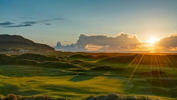 A golf course with rolling hills and a sunset in the background.