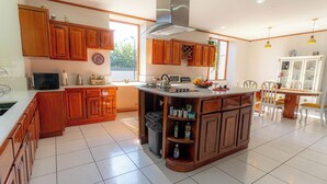 A kitchen with wooden cabinets, a central island, and a dining area with chairs. - Casa Familiar la Tortuga (San Pablo)