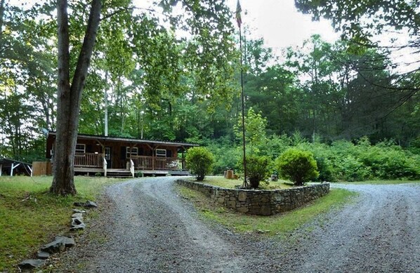 Un chalet rustique doté d’une véranda, entouré d’un mur de pierres et d’une végétation luxuriante.