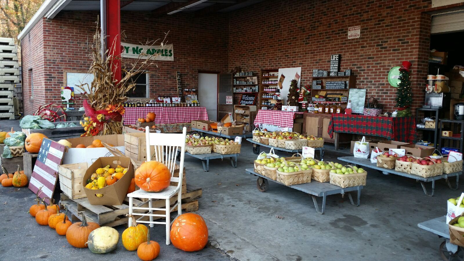 A market stall with pumpkins, gourds, and apples displayed on tables and chairs.