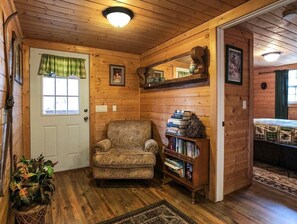 Interior acogedor de una cabaña de madera con un sillón estampado, una estantería y una cama con colcha estampada.