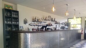 Zona de bar con suelo a cuadros, mostrador de acero inoxidable y estanterías con botellas y vasos.