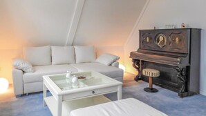 Quarto de estilo loft moderno com um sofá branco, uma mesa de centro de vidro, um banquinho branco e um piano de madeira escura.