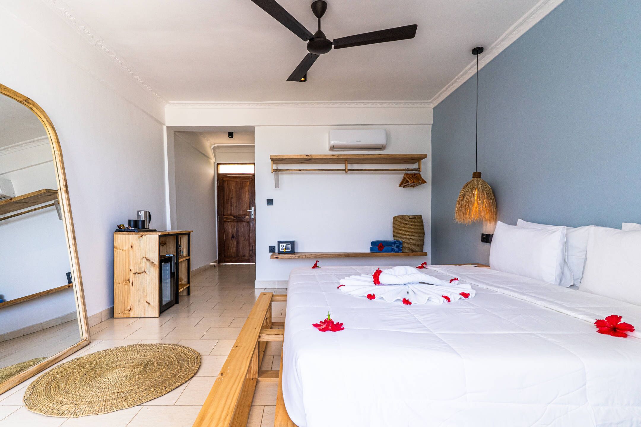 A hotel room with a bed, a ceiling fan, a wooden cabinet, a mirror, and a hanging light fixture.