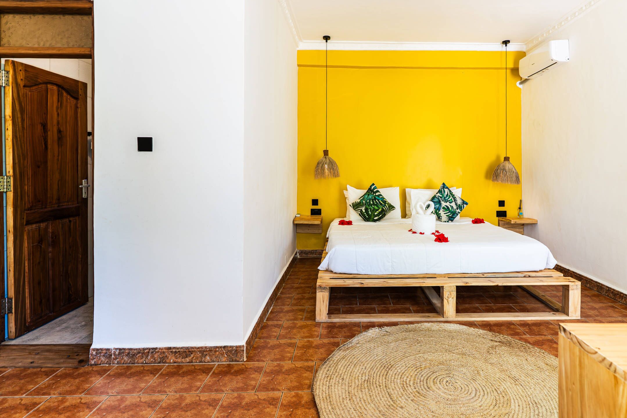 A bedroom with a wooden bed frame, a yellow wall, and a wooden door.