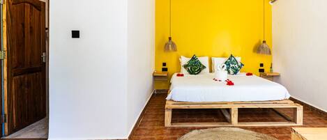 A bedroom with a wooden bed frame, a yellow wall, and a wooden door.