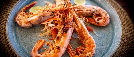Une assiette de crevettes cuites, accompagnée d’un quartier de citron vert et de légumes coupés en julienne.