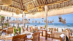 A beachside restaurant with wooden tables and chairs, thatched umbrellas, and hanging lanterns. - Marea Boutique Hotel (Jambiani)