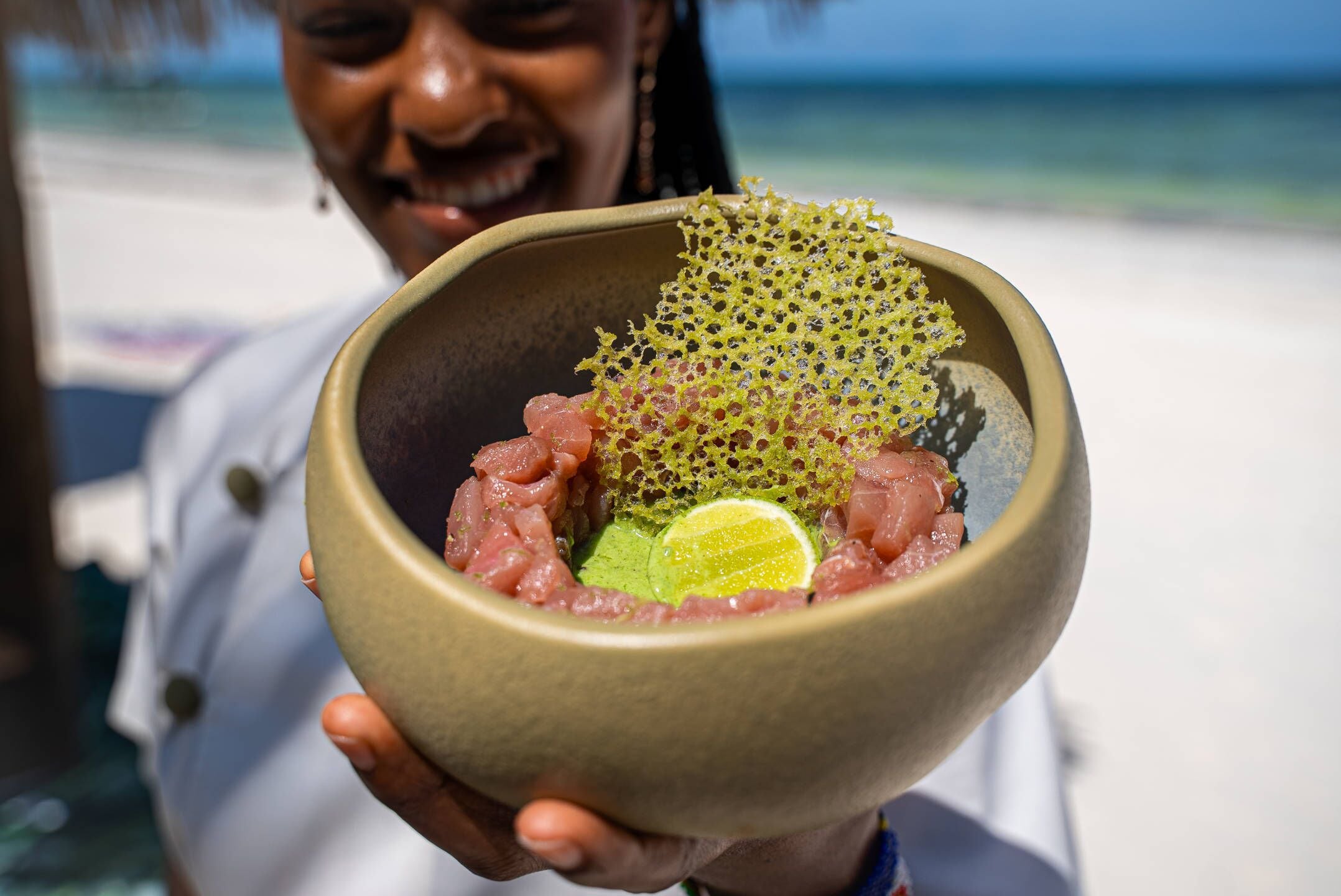A person holding a bowl with raw fish and a lime wedge.
