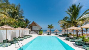 A pool area with lounge chairs and umbrellas, surrounded by palm trees and a view of the beach. - Marea Boutique Hotel (Jambiani)