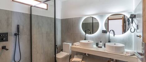 Un baño moderno con ducha acristalada, lavabo blanco y un espejo grande.
