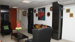 Un hall con un sillón negro, una mesita de centro y un sofá con cojines de colores. Se observan obras de arte enmarcadas en las paredes y una escalera al fondo.