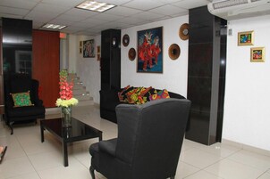 Un hall con un sillón negro, una mesita de centro y un sofá con cojines de colores. Se observan obras de arte enmarcadas en las paredes y una escalera al fondo.