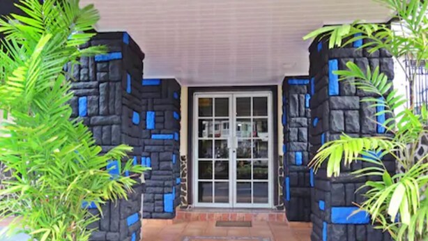 Entrada de un edificio con suelo de baldosas, puerta de cristal y dos plantas en macetas.