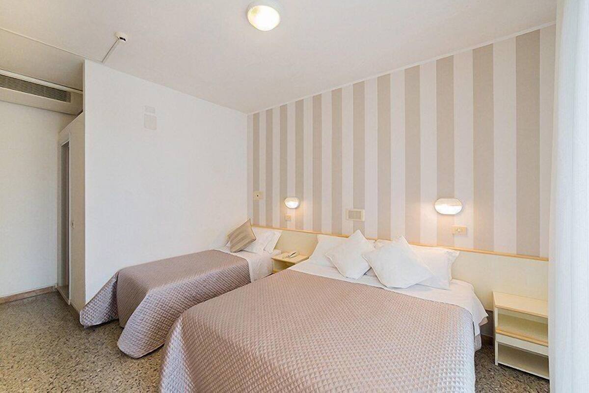 Habitación de hotel con dos camas, un escritorio pequeño y una lámpara fijada a la pared.