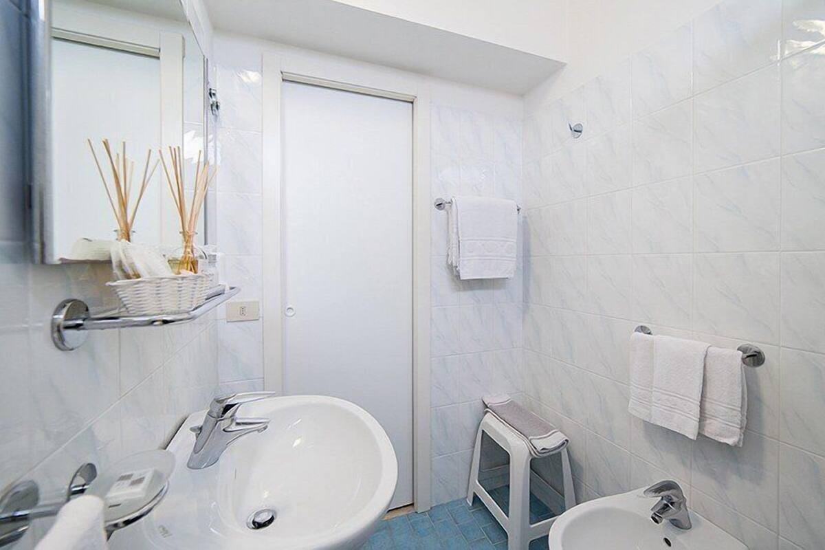 Un baño con lavamanos, bidé y espejo. Hay dos toallas blancas colgadas en la pared.
