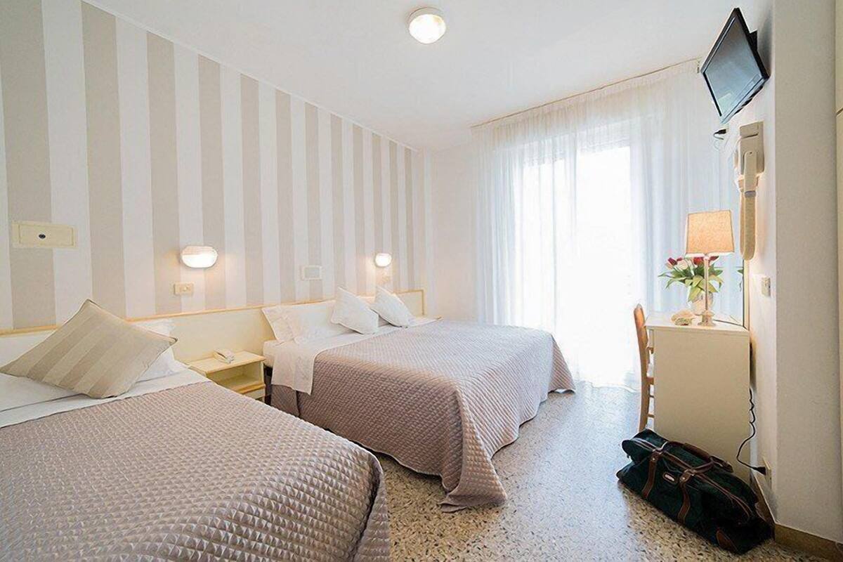 Habitación de hotel con dos camas, televisión, escritorio con lámpara y ventana con cortinas.