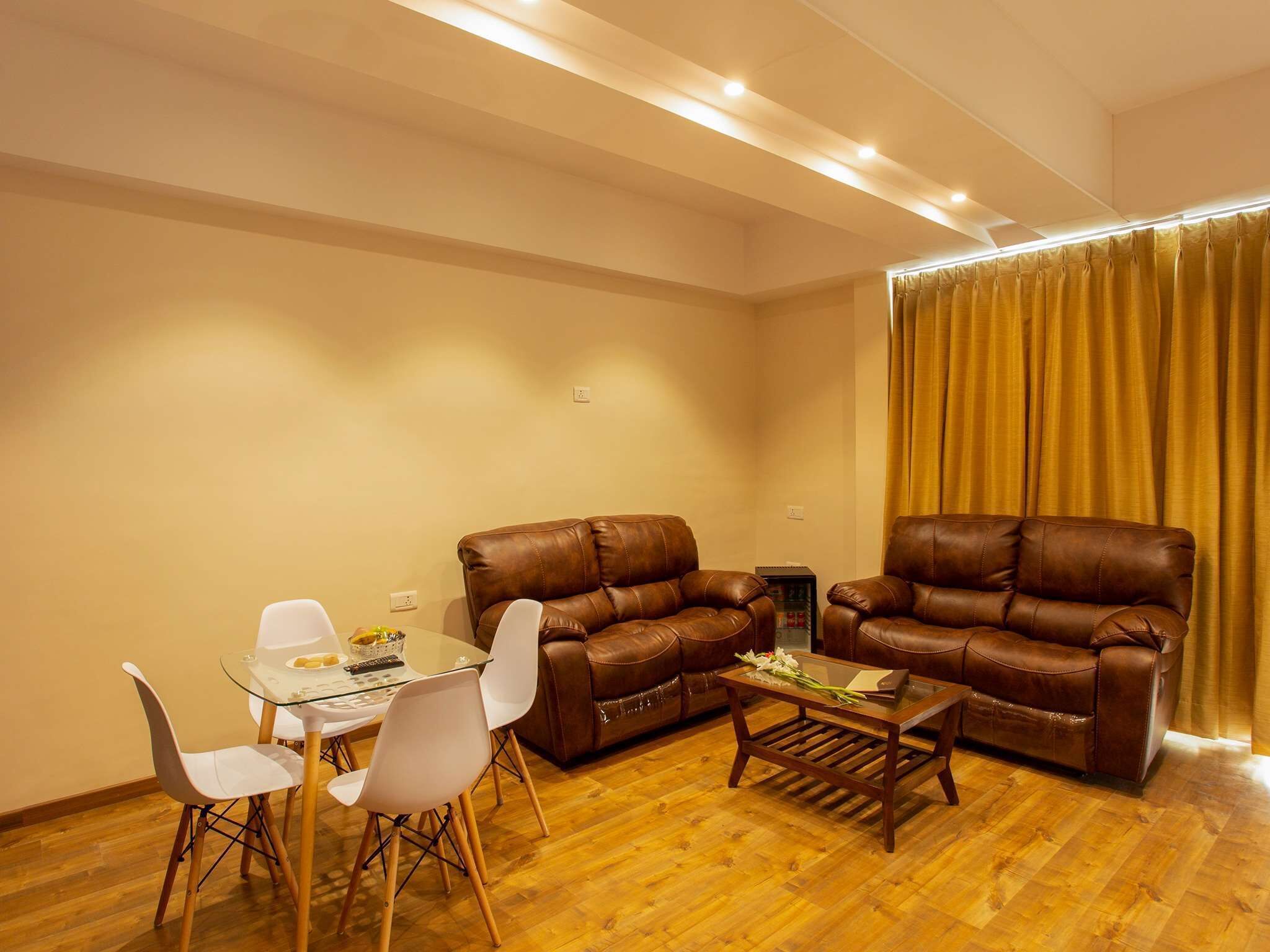 A living room with a brown leather sofa, a glass coffee table, and white chairs.