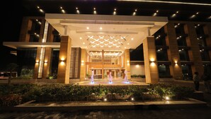 A modern hotel entrance with a well-lit facade, a central water feature, and a clear view of the entrance doors. - Sarovar Portico Somnath (Veraval)