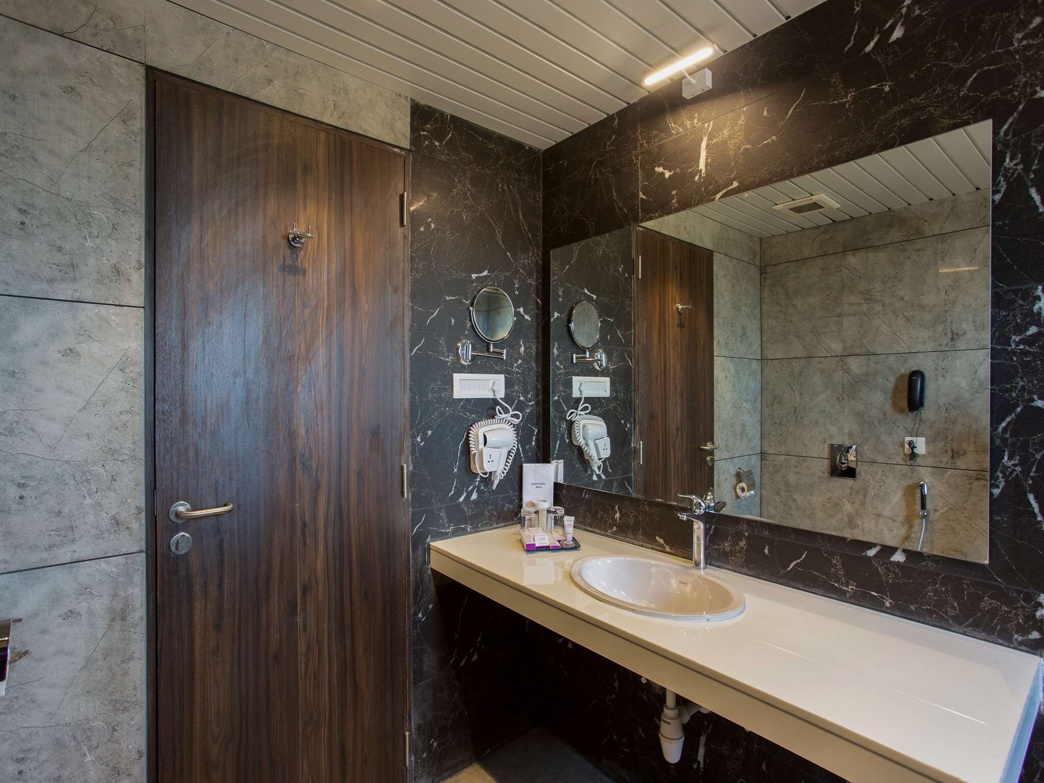 Un baño moderno con tocador de mármol, un espejo grande y una puerta de madera.