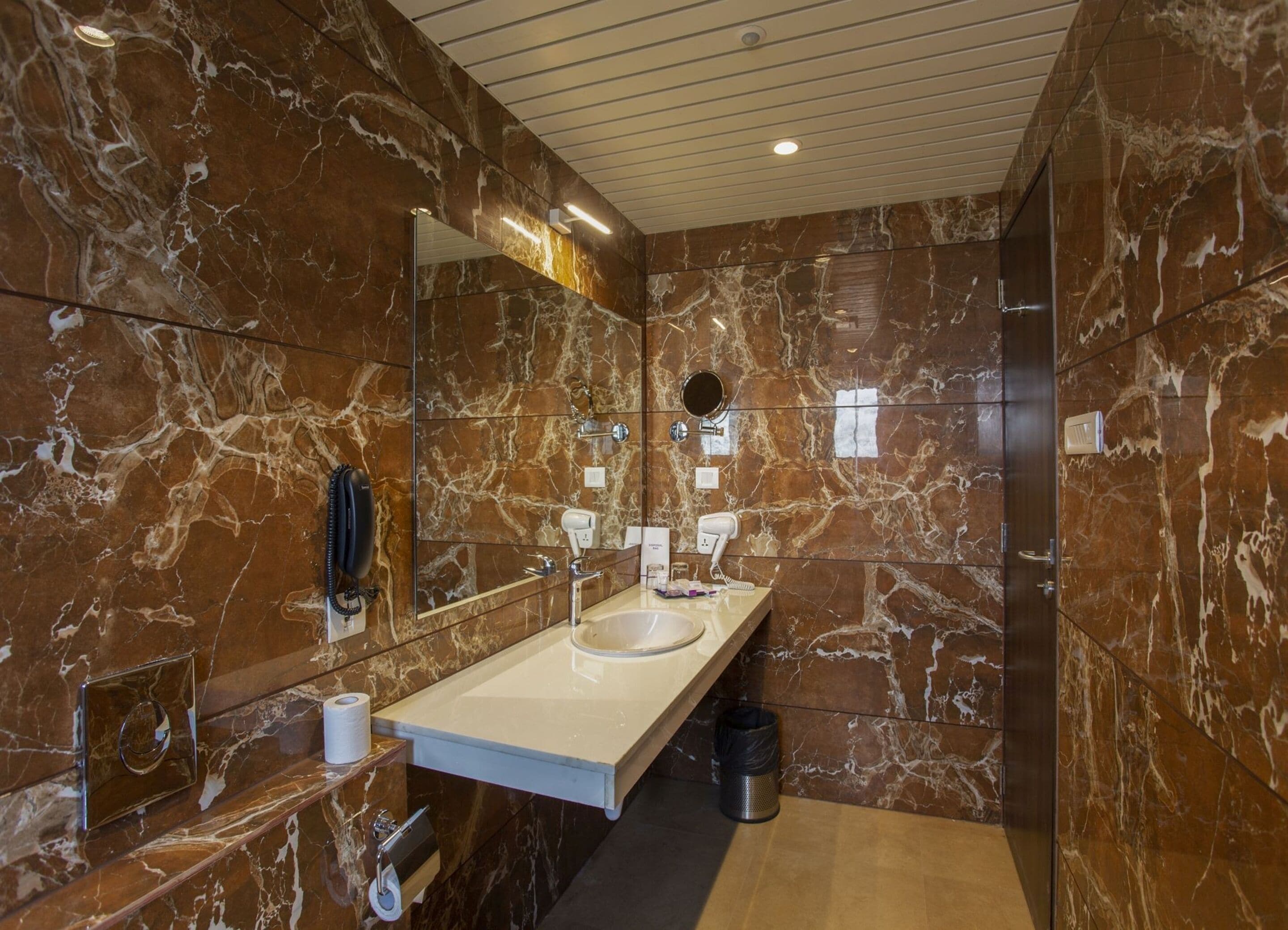 A modern bathroom with a marble wall, a large mirror, a sink, and a hairdryer.