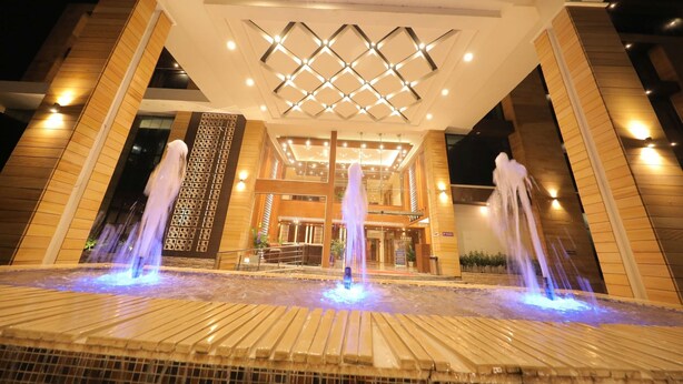 A hotel entrance with a central fountain, a modern ceiling design, and a symmetrical facade. - Sarovar Portico Somnath (Veraval)