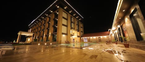 Un hotel moderno con un amplio espacio exterior, piscina y una entrada bien iluminada.