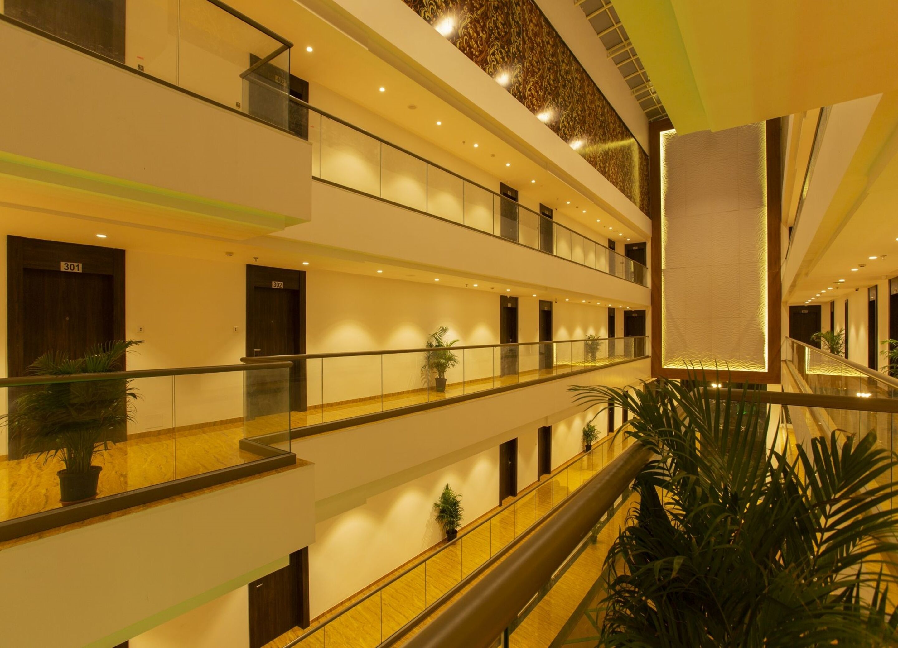 A multi-level hotel interior with glass railings, potted plants, and a warm, yellow-lit ambiance.