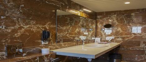 A modern bathroom with marble walls, two sinks, a large mirror, and a phone mounted on the wall.