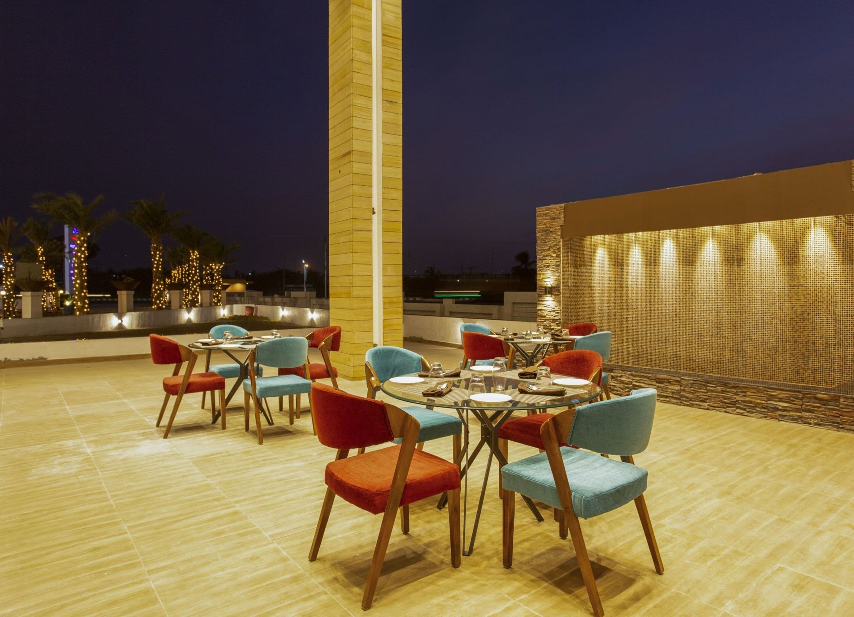 An outdoor dining area with round tables and chairs, a tall pillar, and a decorative wall.