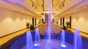 A hotel corridor with a central fountain, multiple floors, and a modern design. - Sarovar Portico Somnath (Veraval)