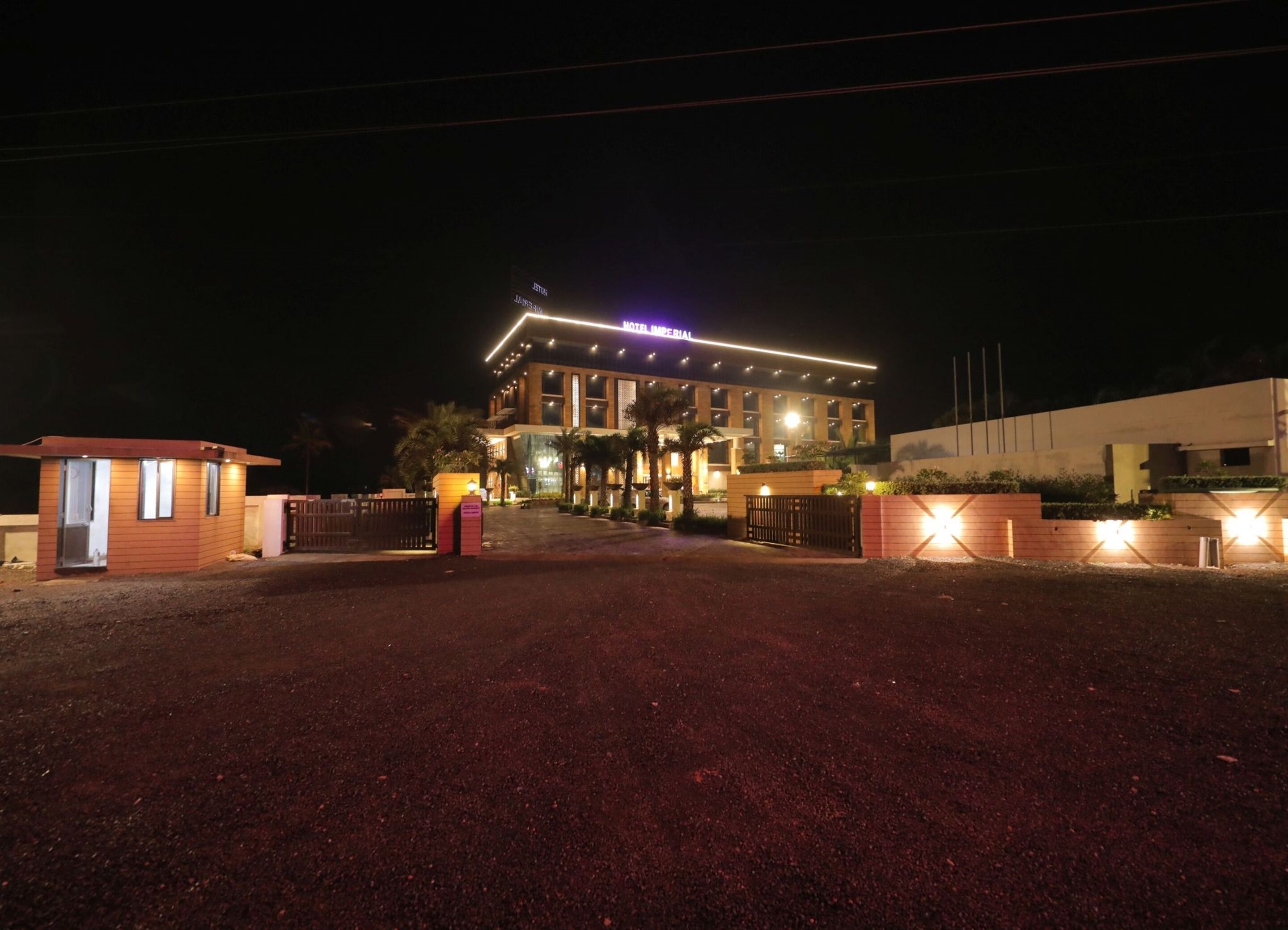 A modern hotel with a prominent entrance, a well-lit facade, and a gated driveway.