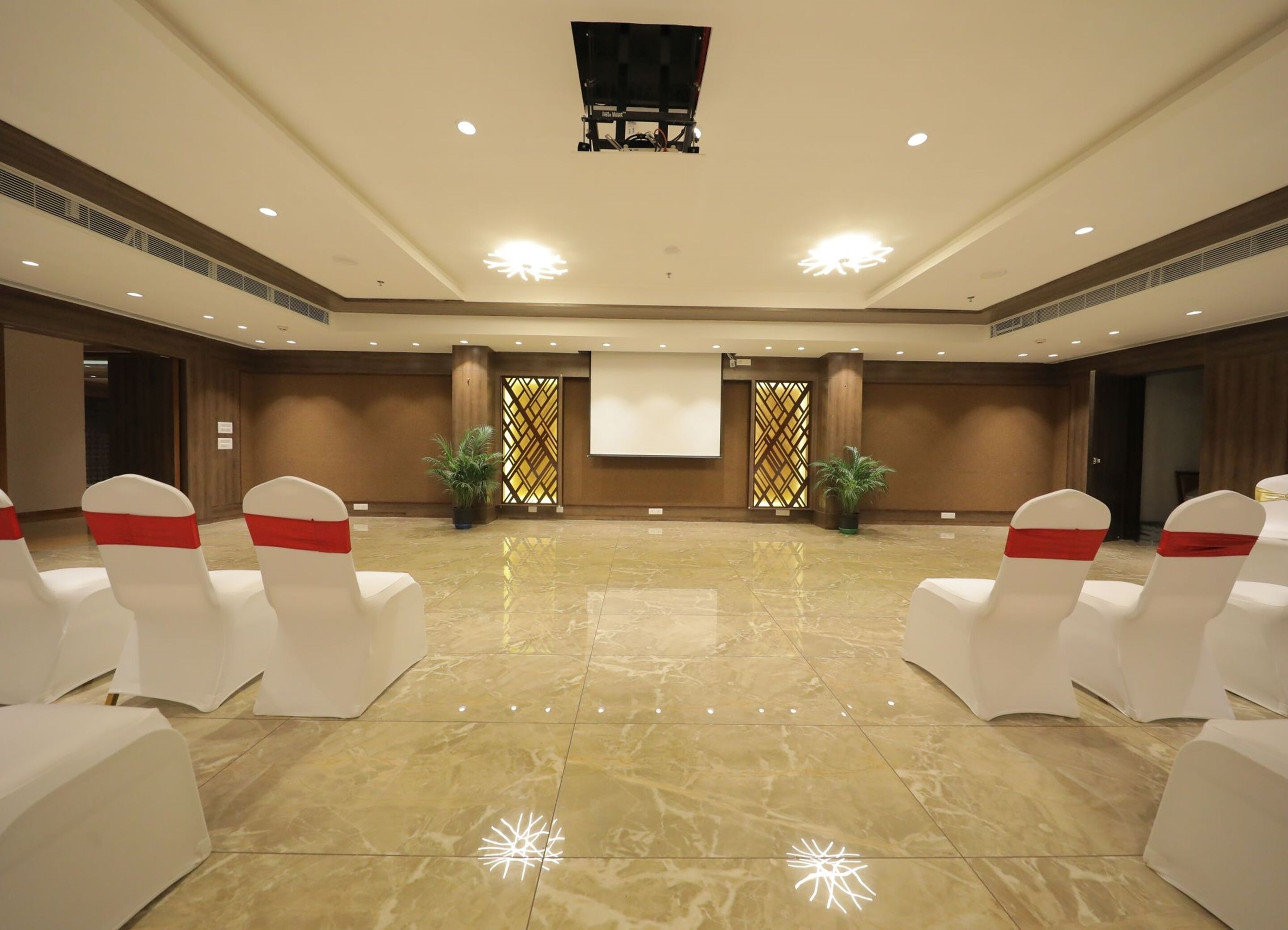 A spacious conference room with white chairs and red sashes, a large screen, and a polished marble floor.