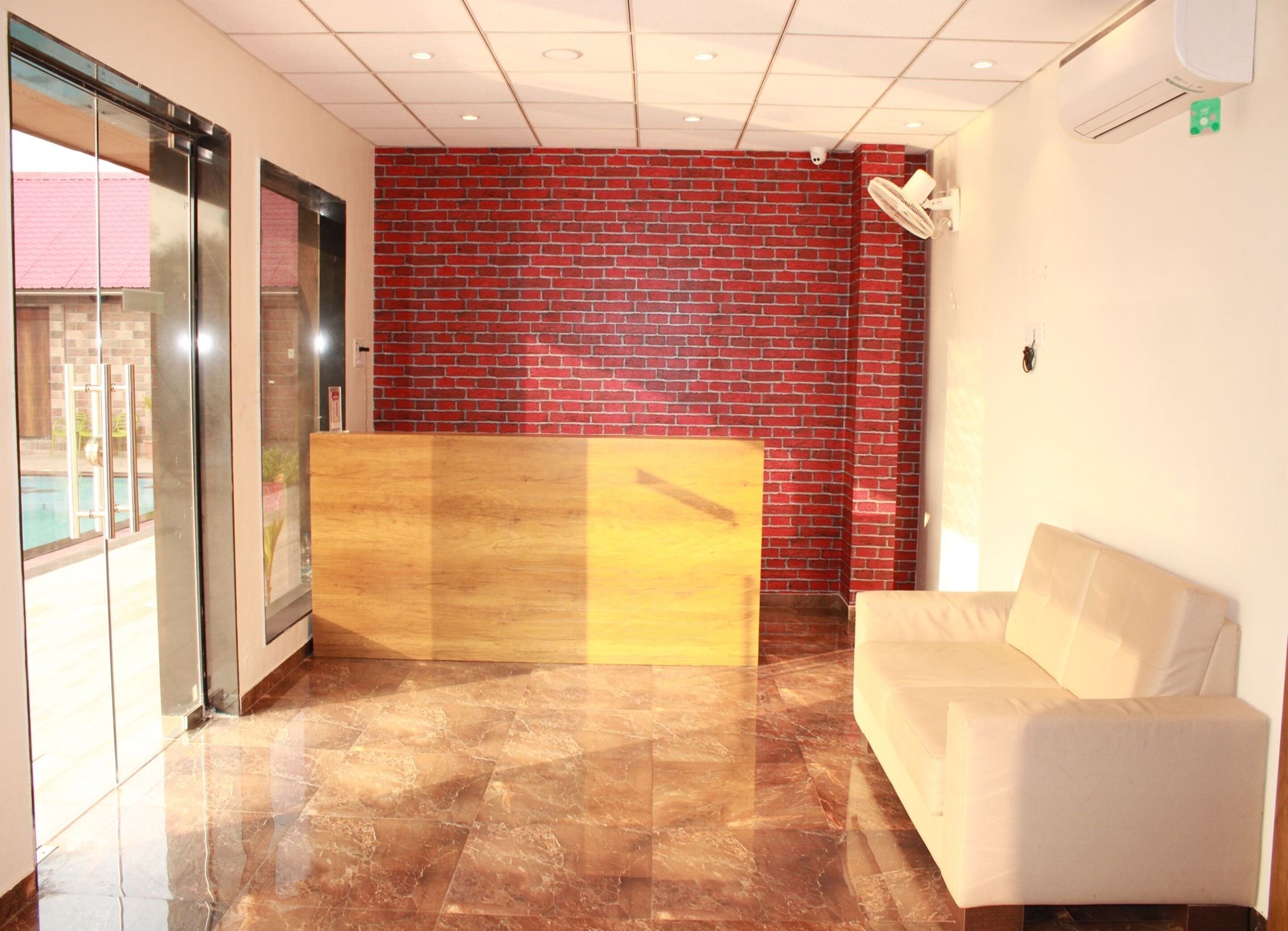 A reception area with a red brick wall, a reception desk, a white sofa, and a glass door leading outside.
