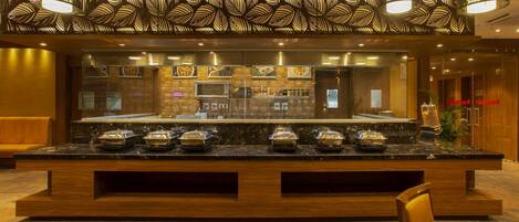 A hotel lobby with a marble reception desk, a seating area, and a buffet counter with covered food items.