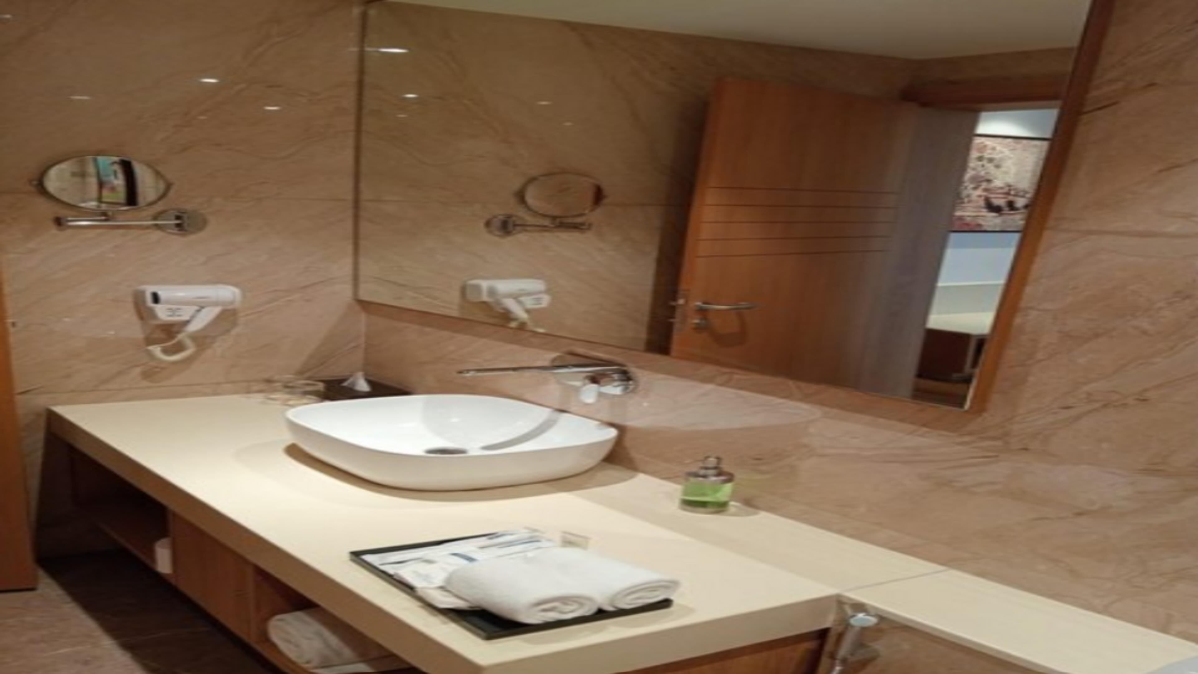 A modern bathroom with a large mirror, a white sink, and a towel rack.
