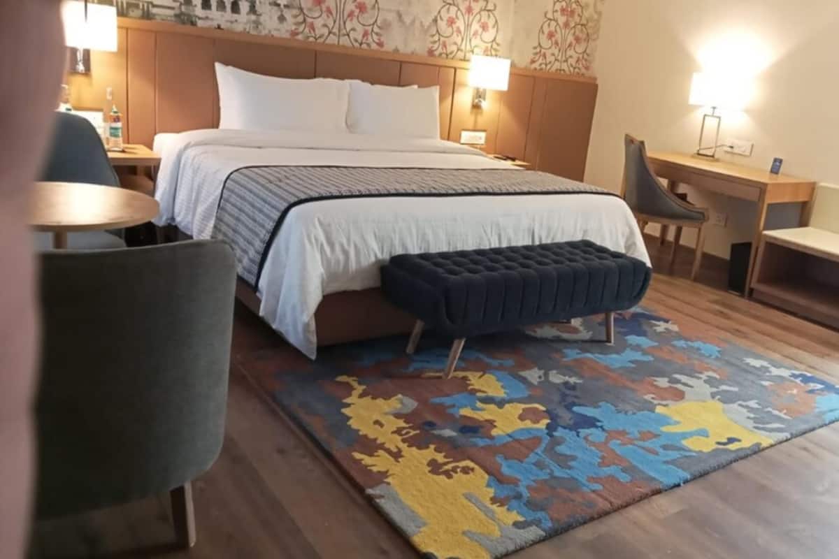 A hotel room with a bed, bedside tables, a desk, a chair, and a bench.