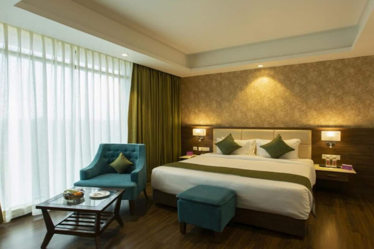 A hotel room with a bed, a chair, a table, and a large window with curtains.