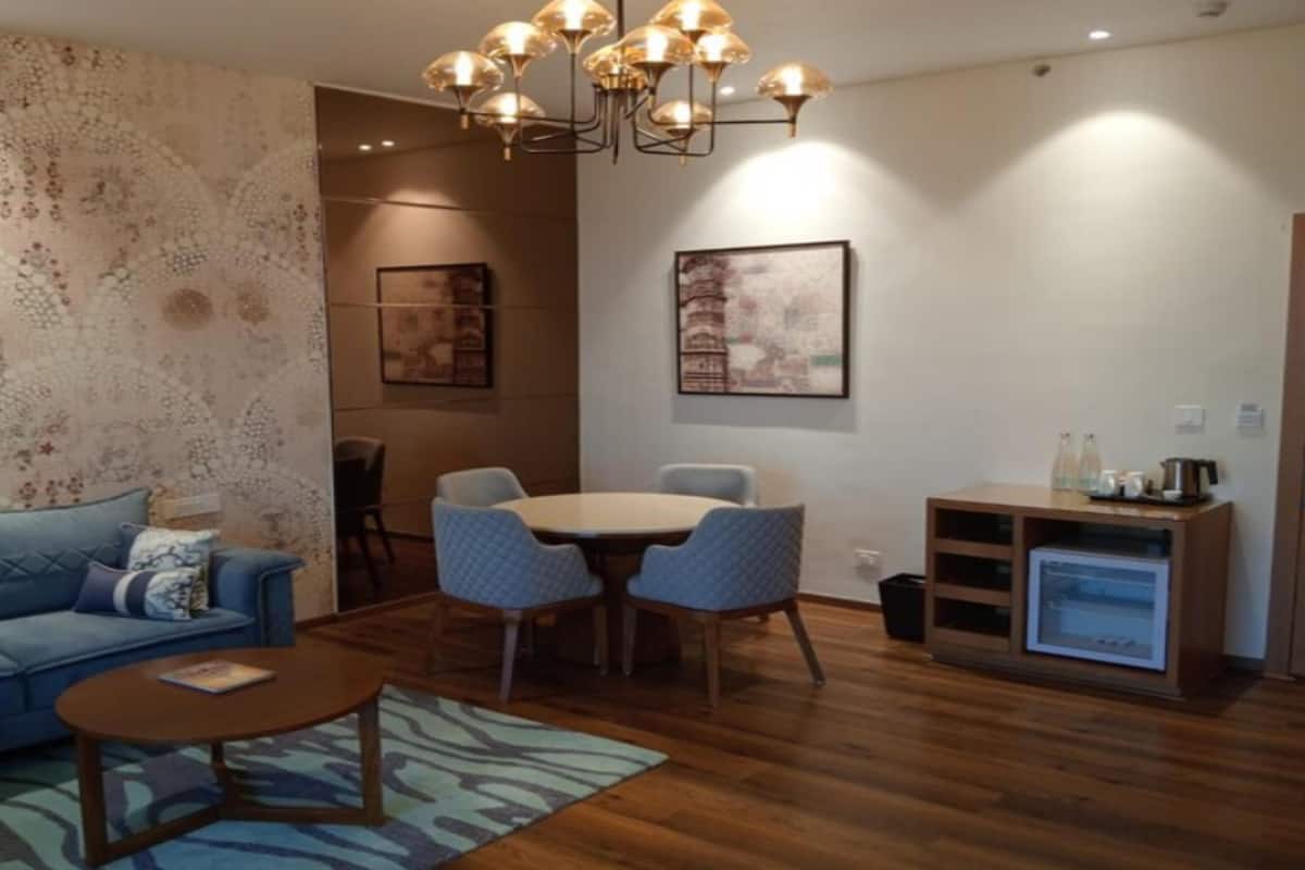 A living room with a sofa, coffee table, dining table with chairs, a patterned wall, and a small kitchenette.