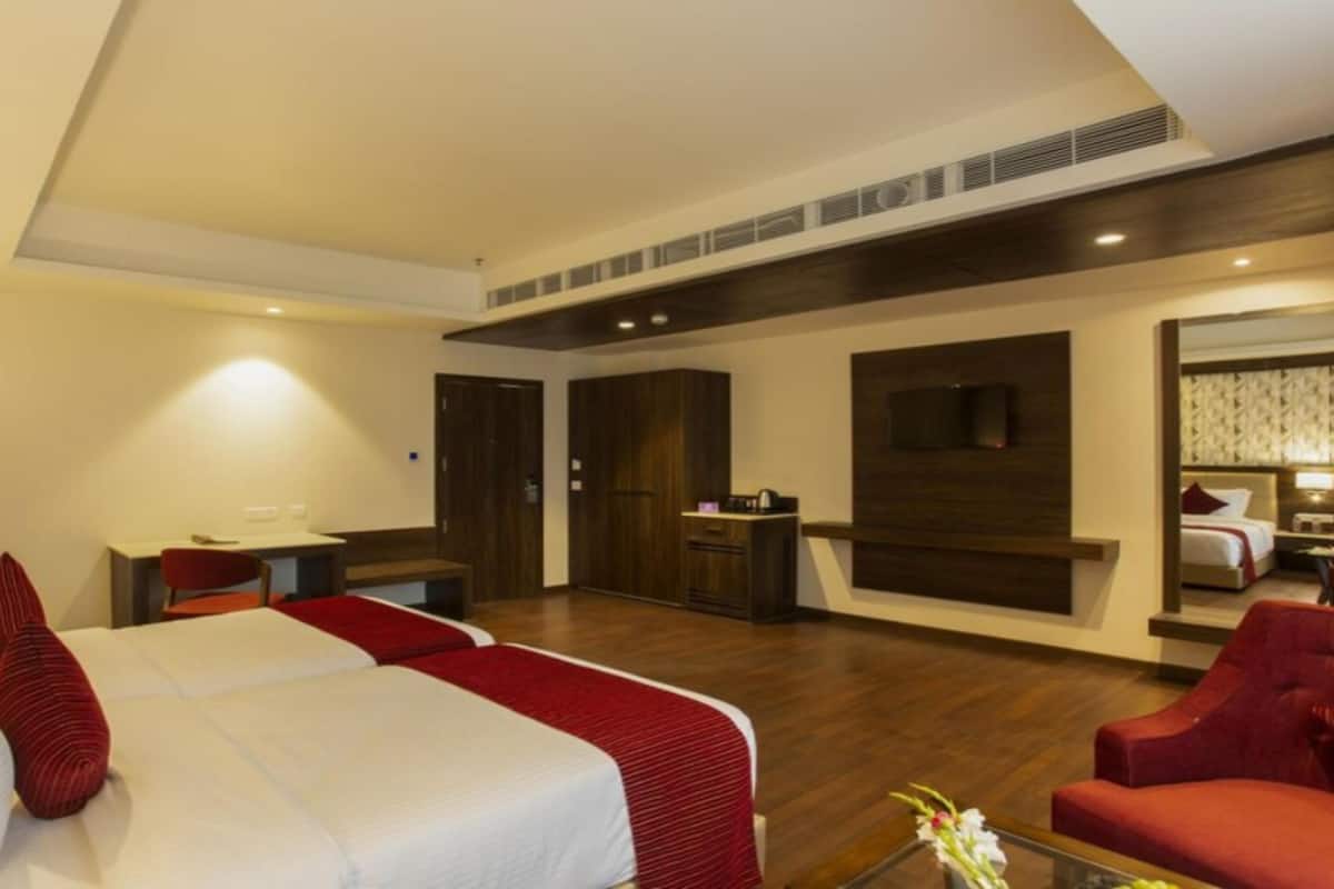 A hotel room with two beds, a desk, a chair, and a TV.