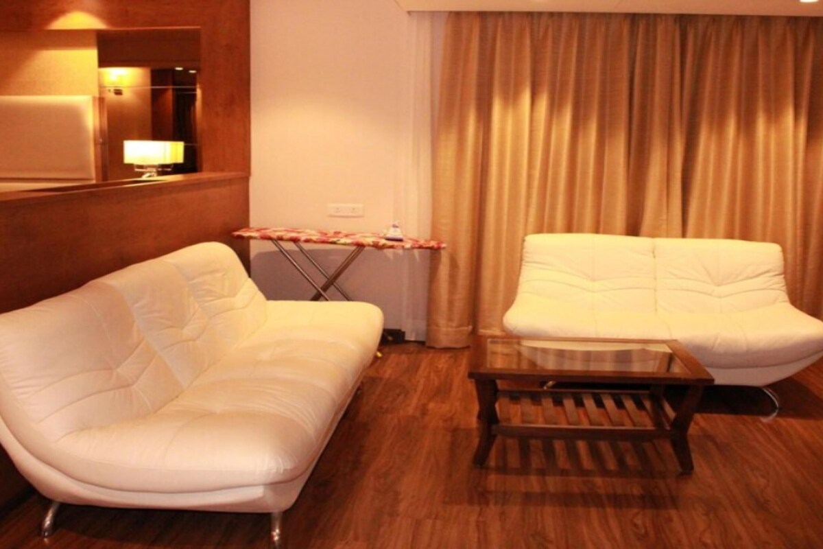 A hotel room with a white sofa, a smaller white armchair, and a wooden coffee table.