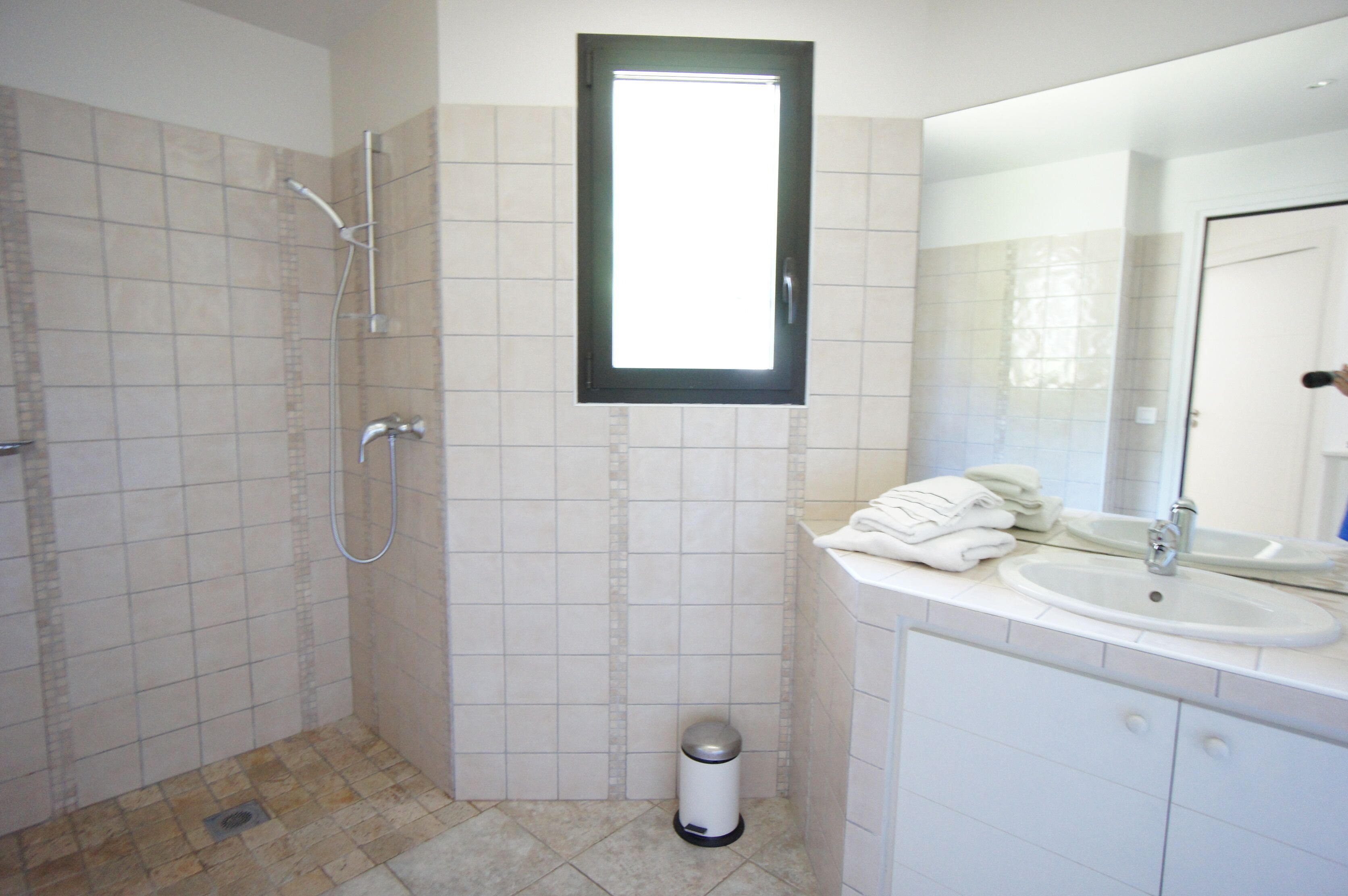 Une salle de bain avec une douche, un lavabo, un miroir et une fenêtre.