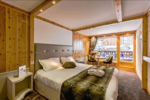 A bedroom with a bed, bedside table, and a view of the outside balcony. - Hôtel Les Sherpas (Courchevel)