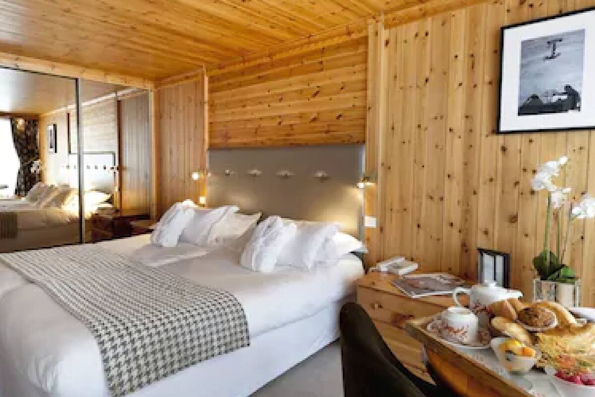A hotel room with a large bed, bedside tables, a mirror, a wooden ceiling, and a framed picture on the wall.