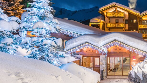 A snow-covered lodge with a wooden entrance and a balcony, surrounded by snow and mountains. - Hôtel Les Sherpas (Courchevel)