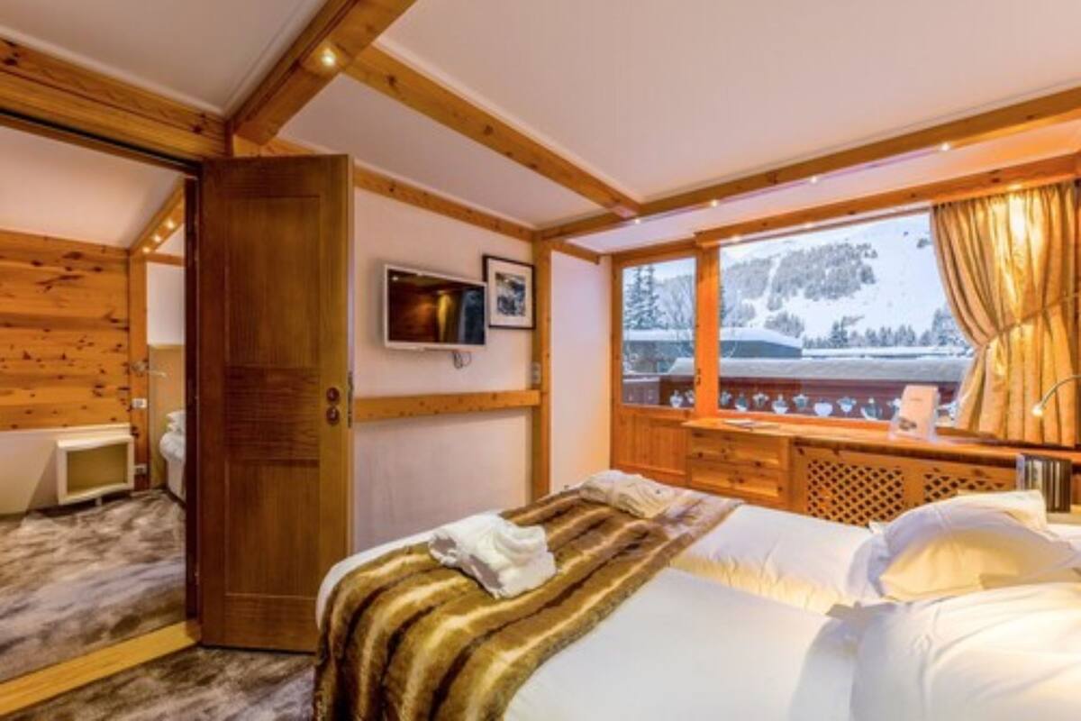 A cozy room with a bed, wooden walls, a television, and a window with a view of trees.