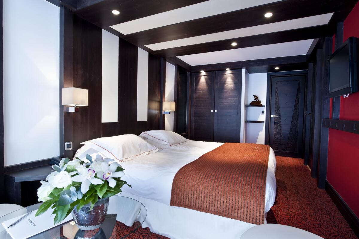 A modern hotel room with a large bed, dark wood paneling, and a red accent wall.