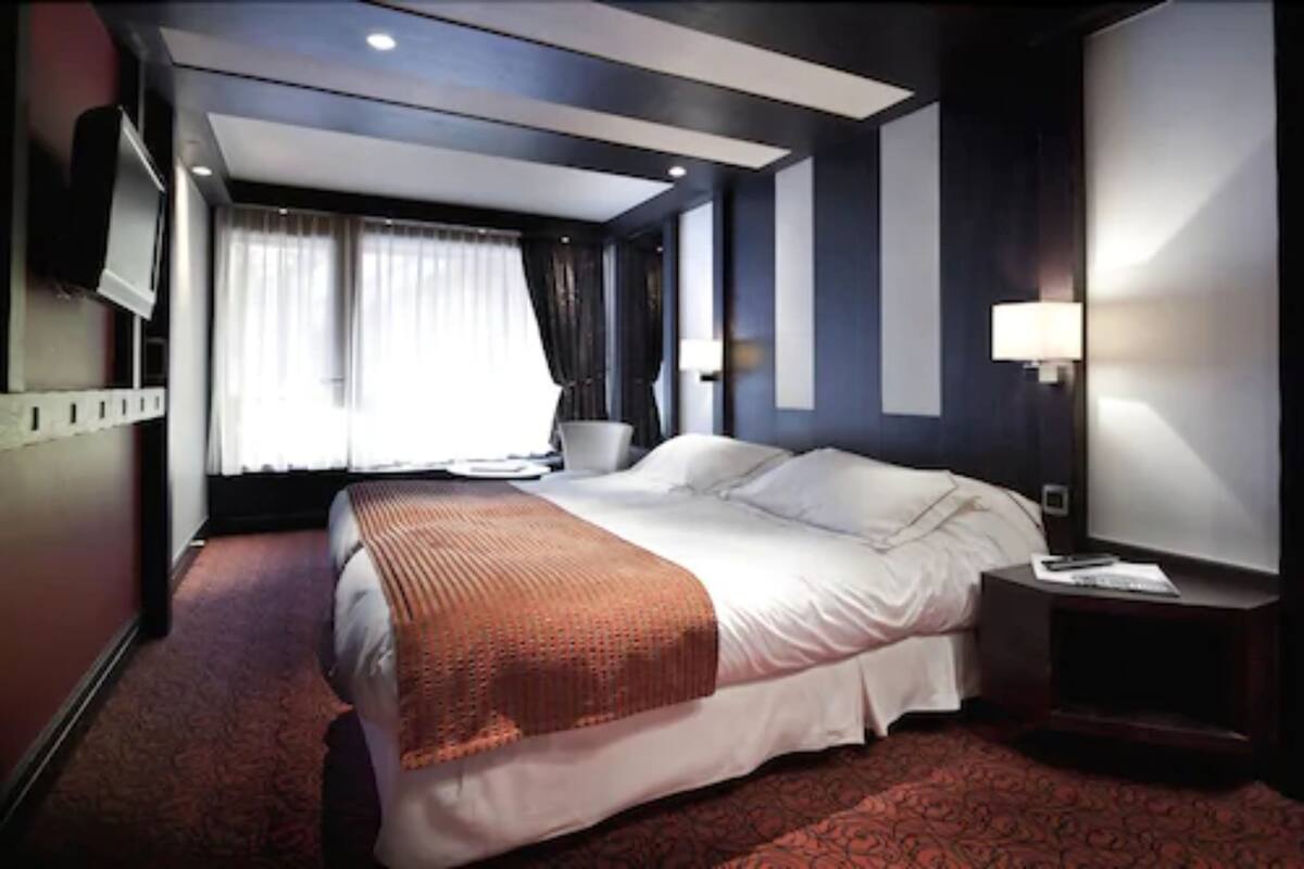 A hotel room with a large bed, a flat-screen TV, a bedside table, and a window with curtains.