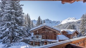 A wooden chalet with a balcony, surrounded by snow-covered trees and mountains. - Hôtel Les Sherpas (Courchevel)
