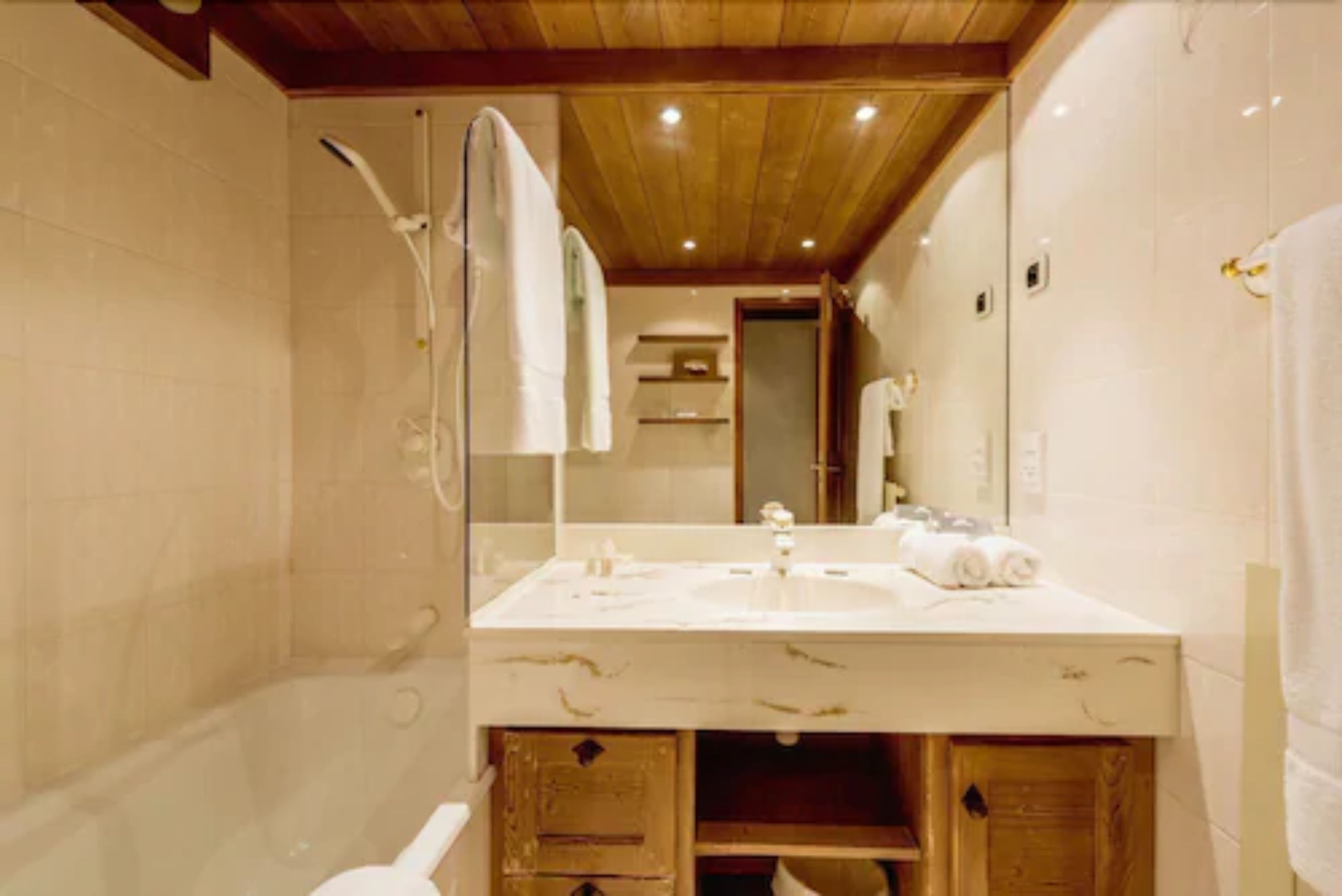 Un baño con techo de madera, un espejo grande, un lavamanos y una ducha.